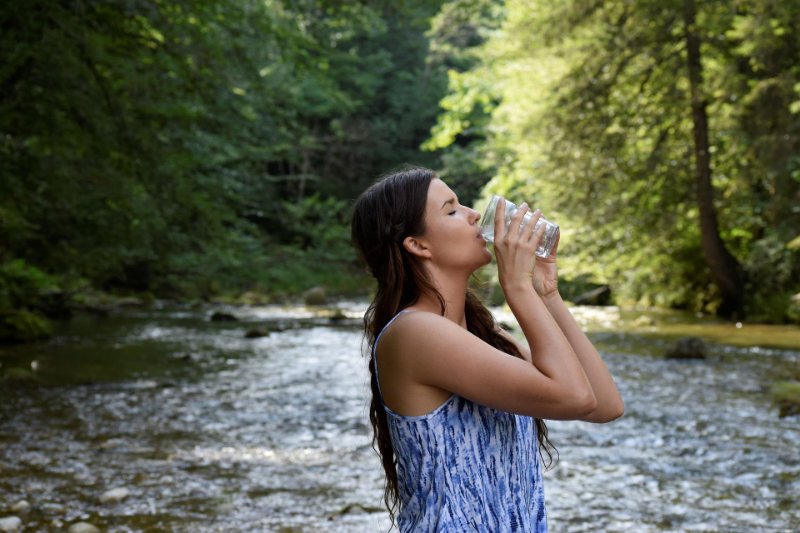a woman drinking water from a glass standing in river