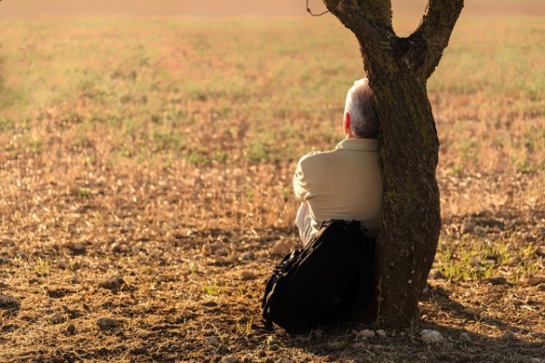 old man leaning relaxed against a tree